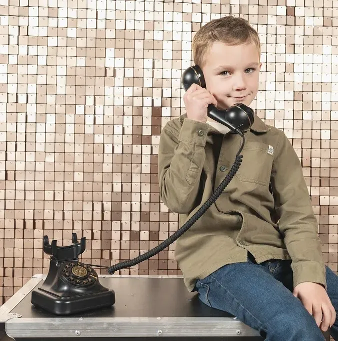 Kind met een retrotelefoon voor een paillettenwand